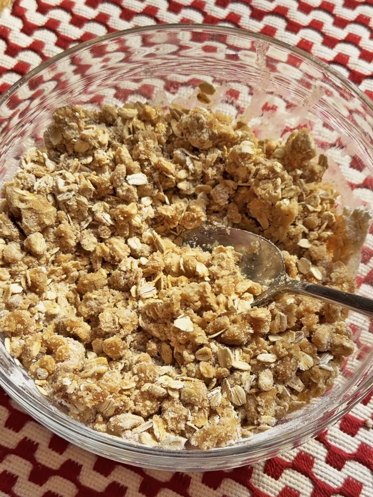 Oat crumble topping in a glass bowl on a red and white patterned cloth.