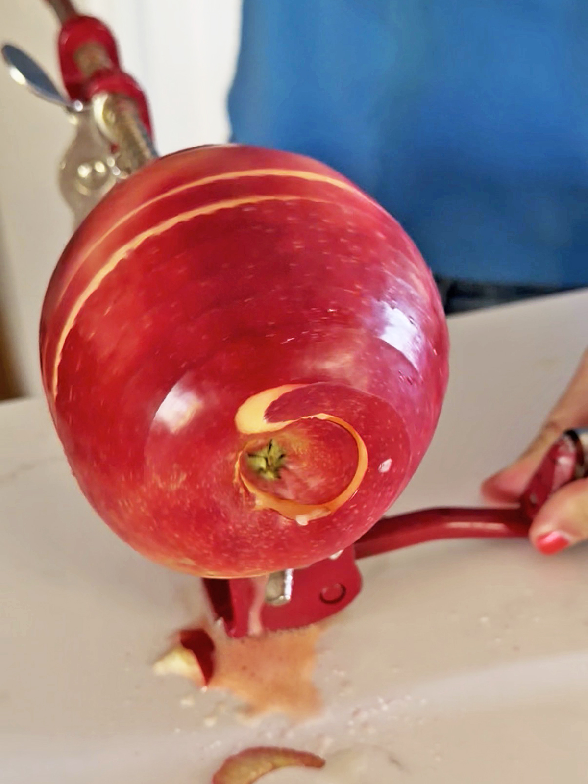 Spiral-cut whole apple on a peeler with a red handle over a kitchen counter.