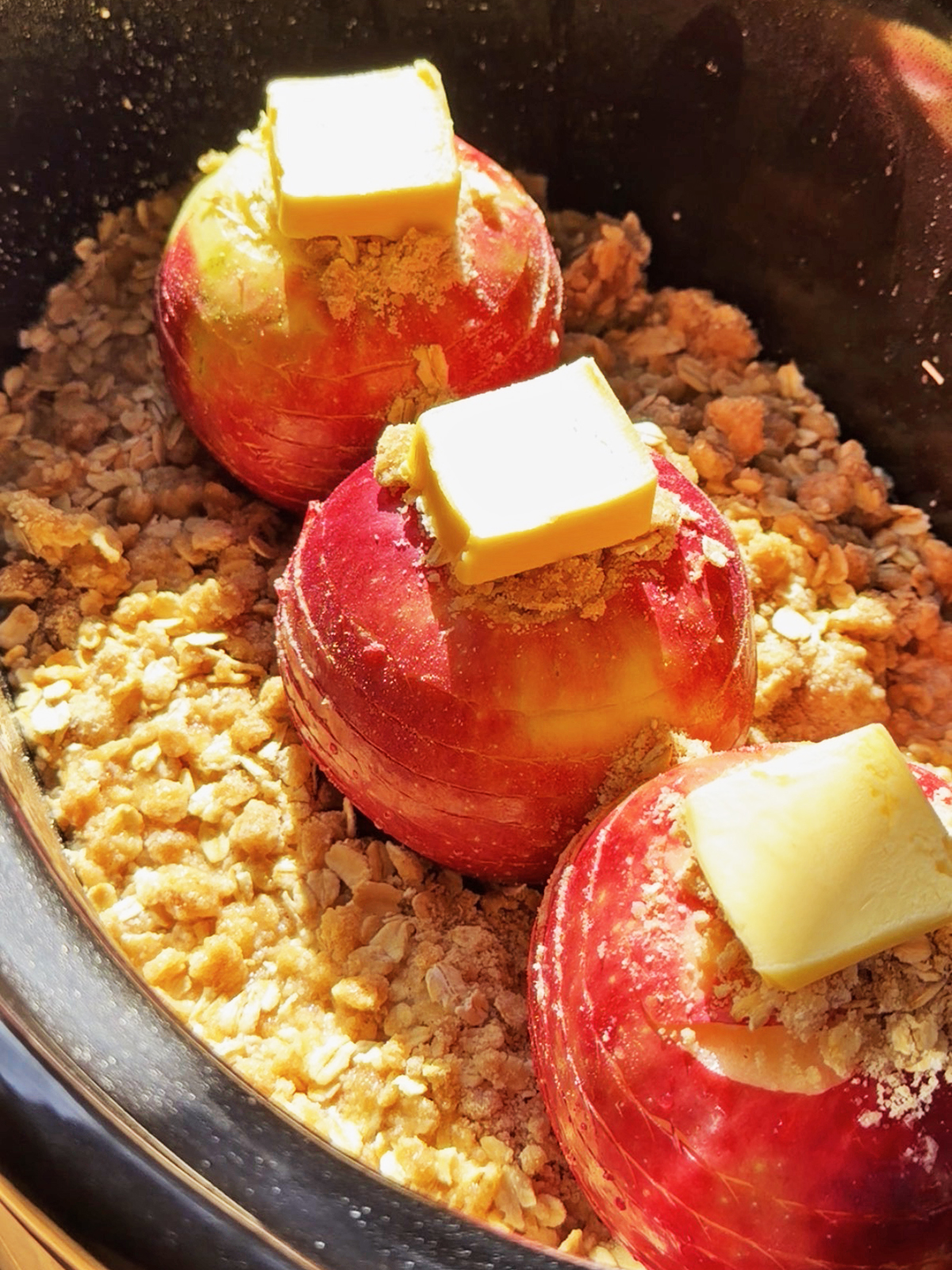 Spiral-cut apples topped with butter and brown sugar in a slow cooker.