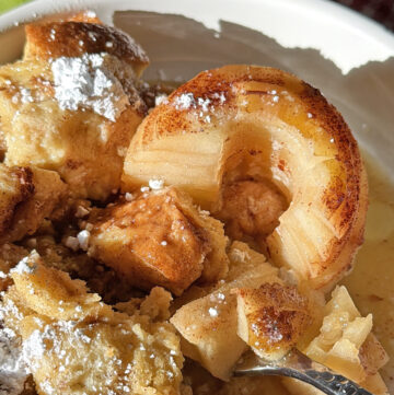 Baked apples with cinnamon and sugar in a white bowl, with a spoon.