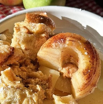 Baked apple and bread pudding with caramelized apple slices in a white dish.