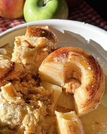 Baked apple and bread pudding with caramelized apple slices in a white dish.