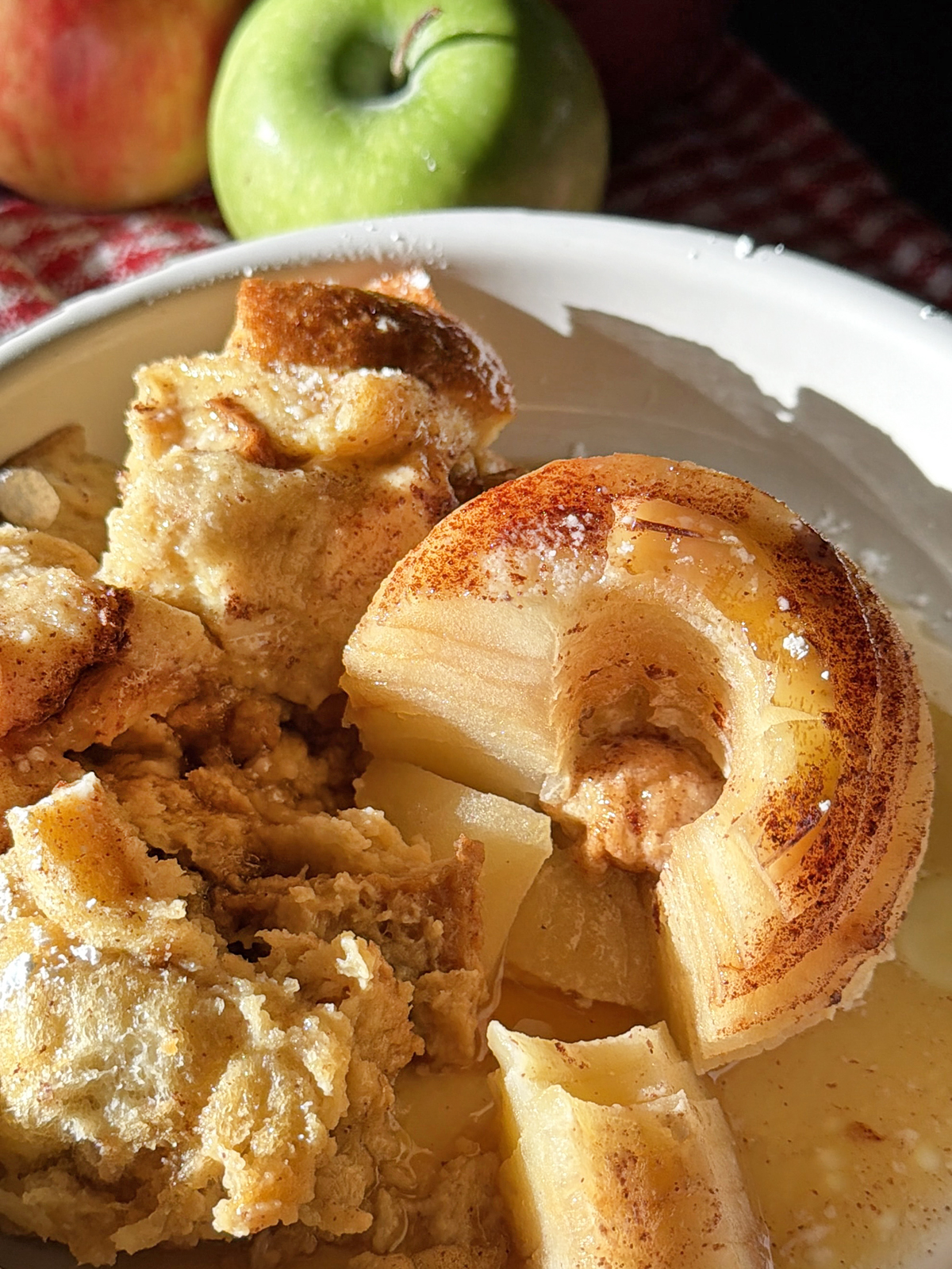 Baked apple and bread pudding with caramelized apple slices in a white dish.