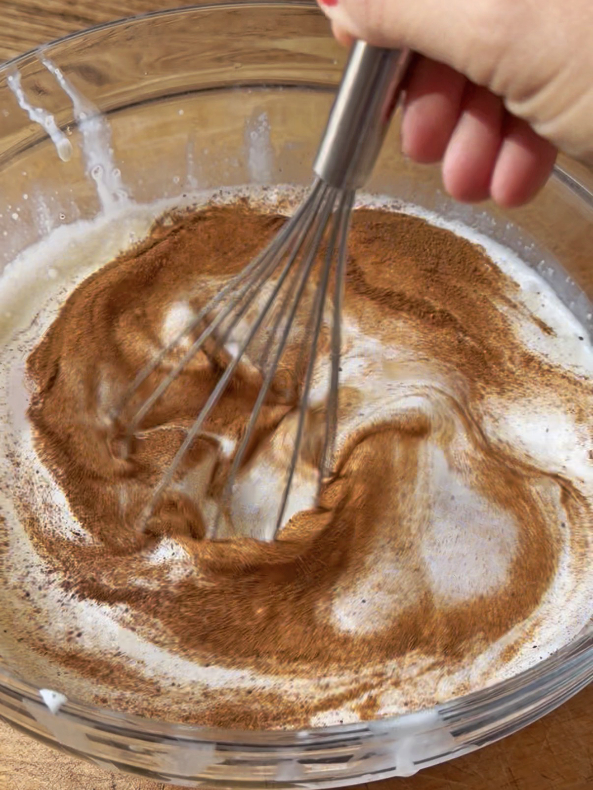 Whisk mixing cinnamon and milk in a glass bowl for French toast.