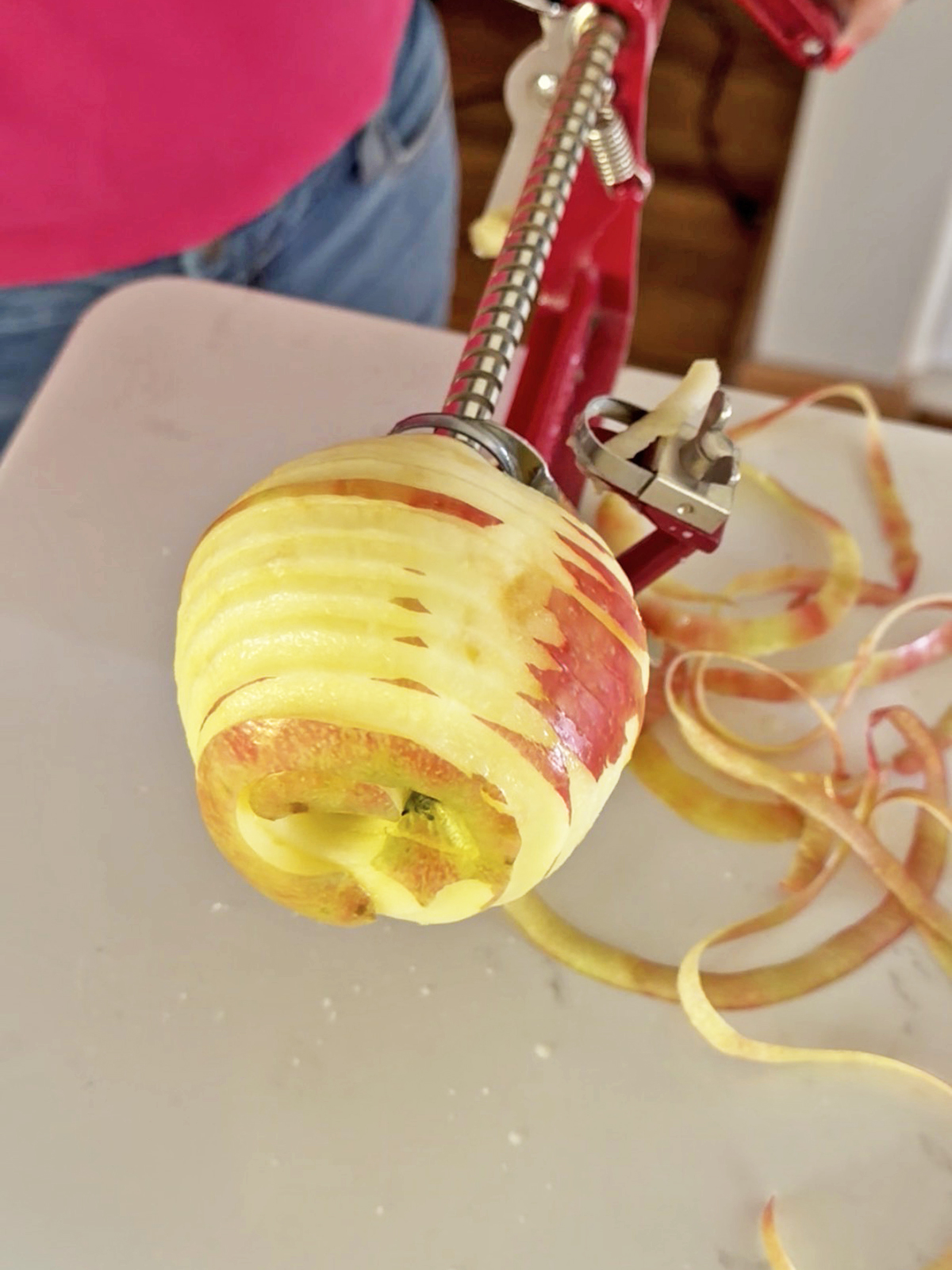 Apple being sliced with a spiralizer, with apple peel ribbons nearby.