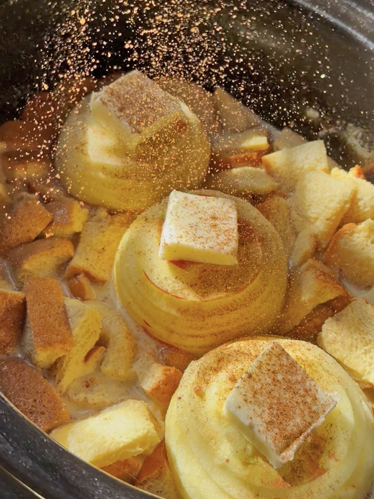 Whole apples with cinnamon and bread cubes in a slow cooker for French toast.