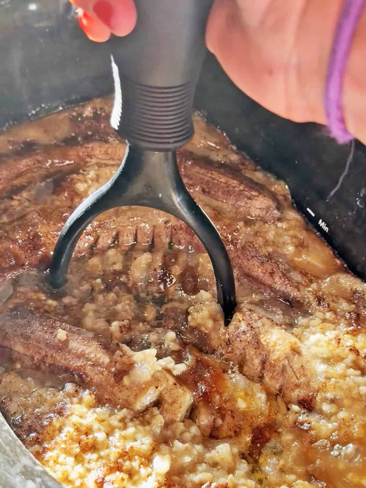 Bacon being cooked in a slow cooker with a meat fork.