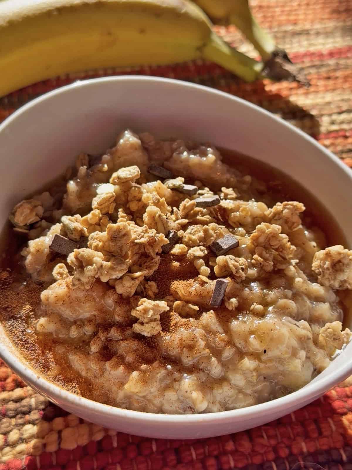 Creamy oatmeal topped with granola and chocolate chips in a white bowl.