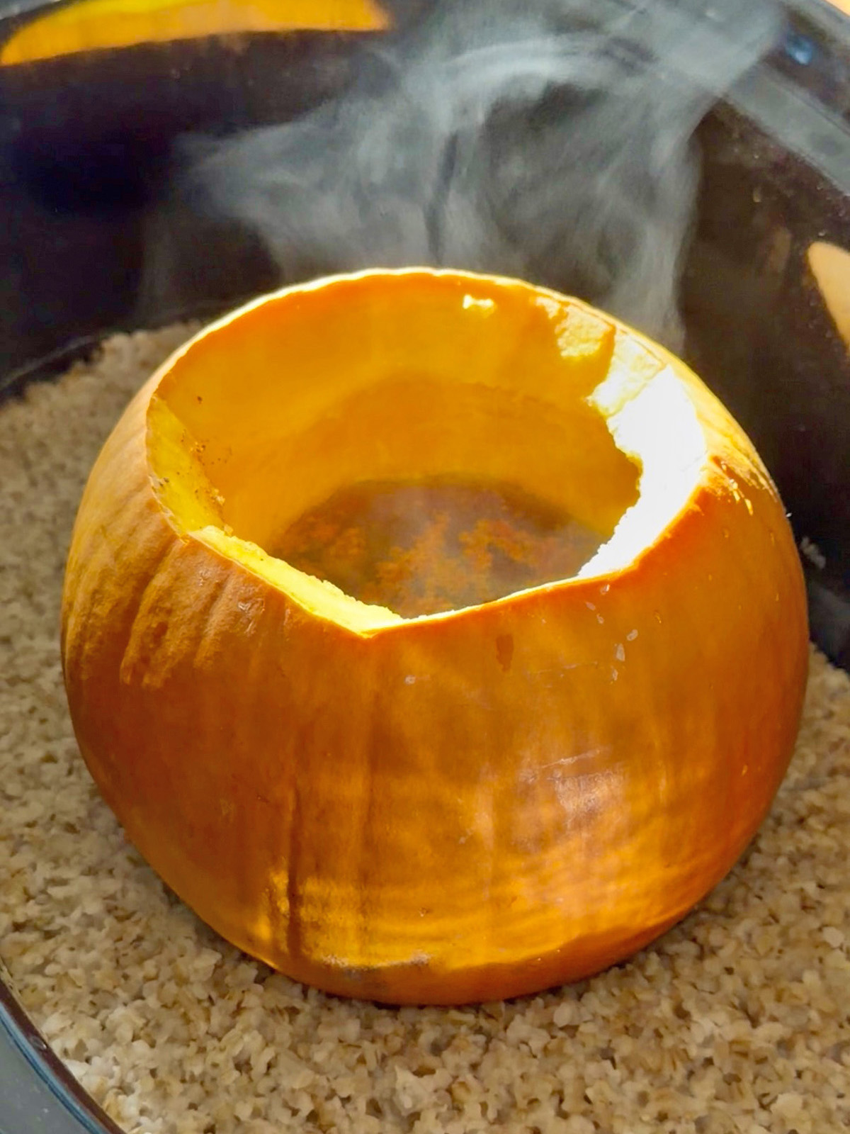 Pumpkin with hollowed-out center steaming over rice or grains.