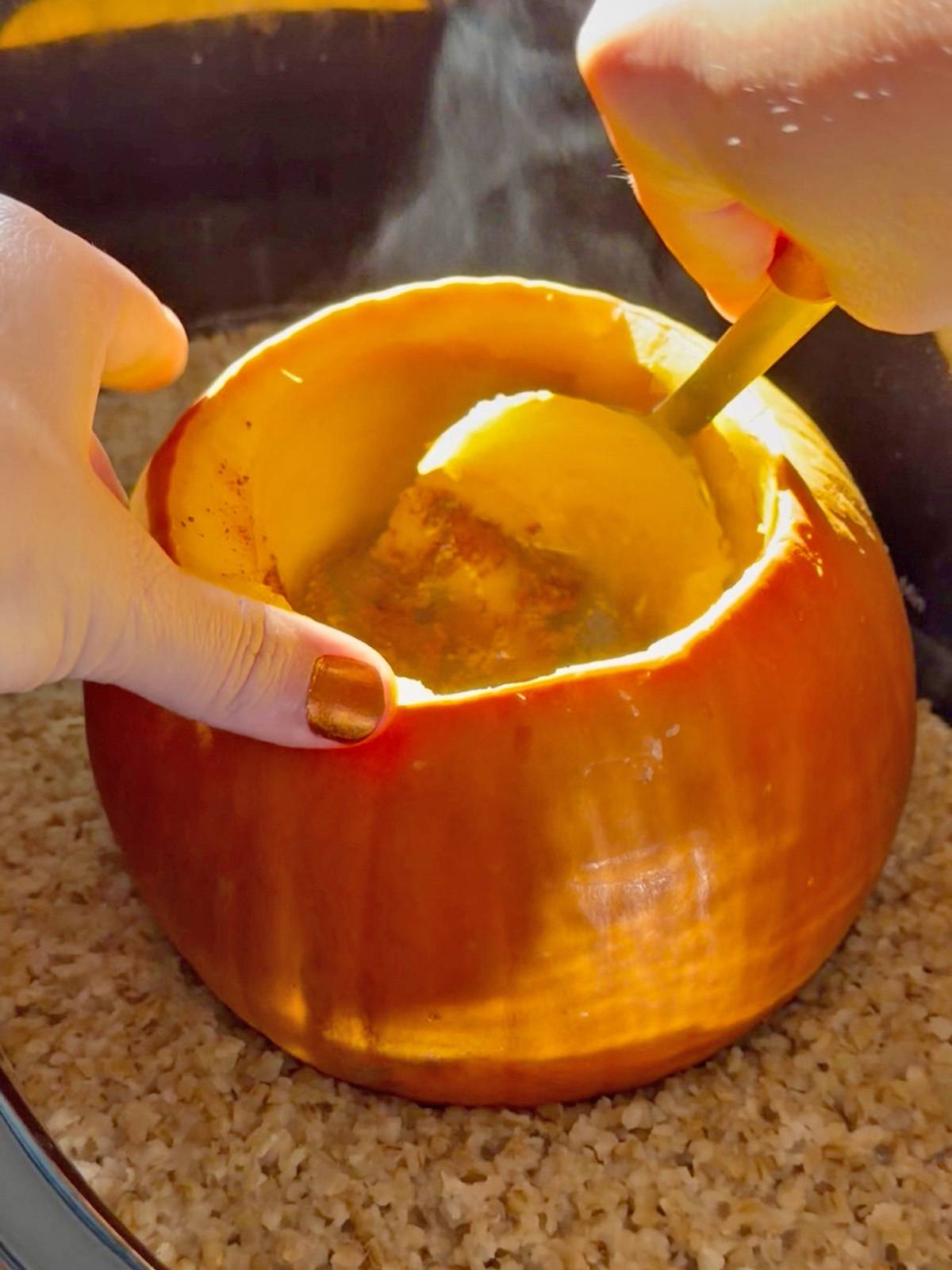 Scooping pumpkin oatmeal from a hollowed-out pumpkin with a spoon.
