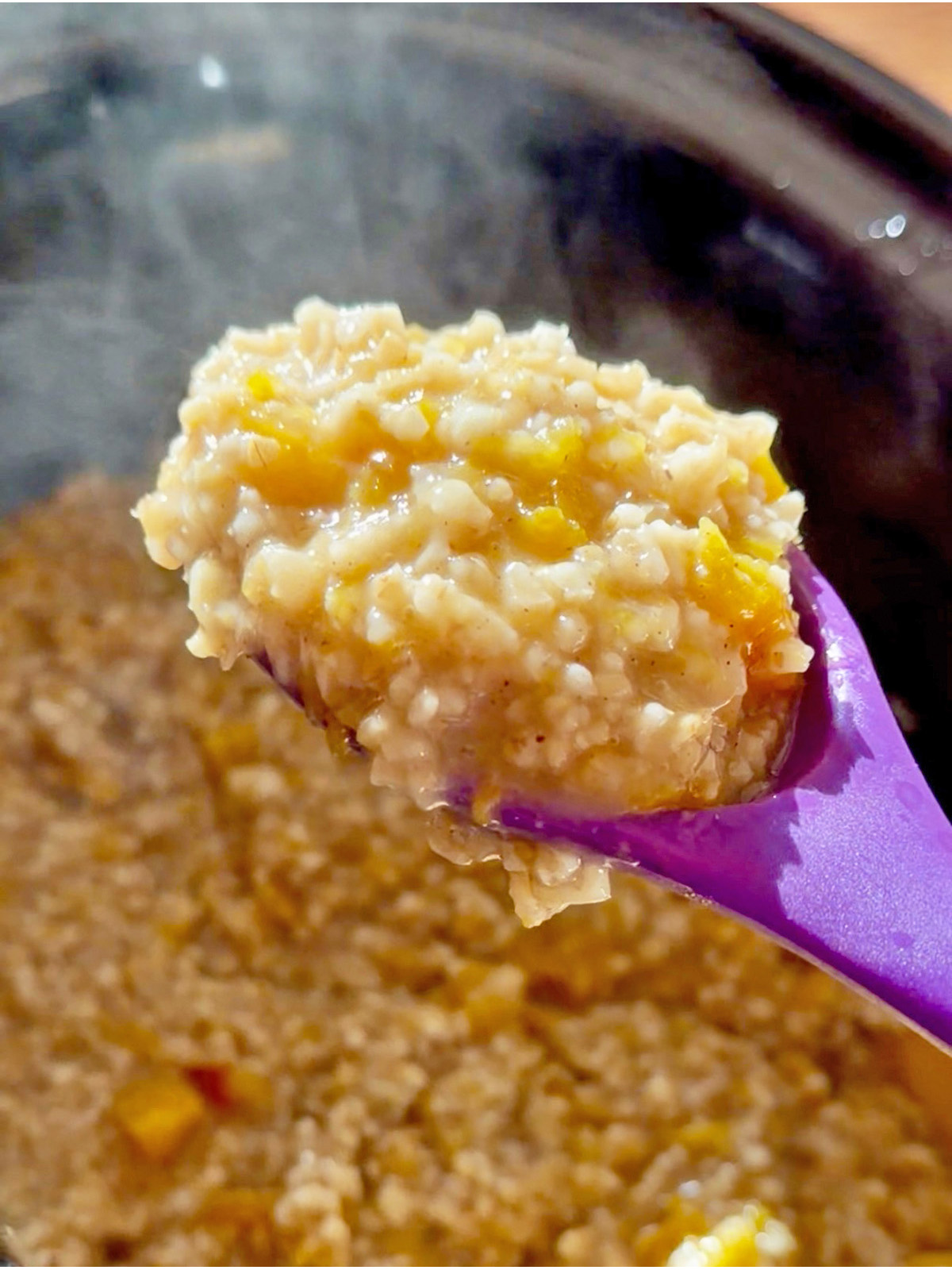 Creamy pumpkin oatmeal with a purple spoon, cooked in a pot.