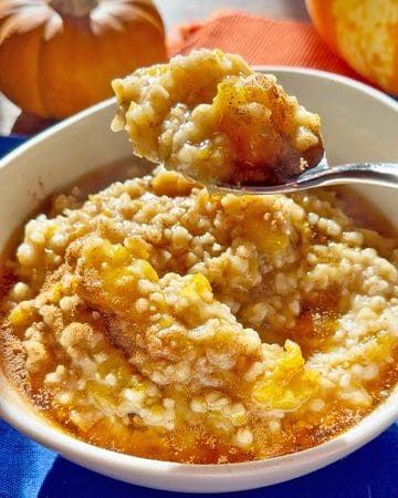 Creamy pumpkin oatmeal topped with cinnamon in a white bowl with a spoon.