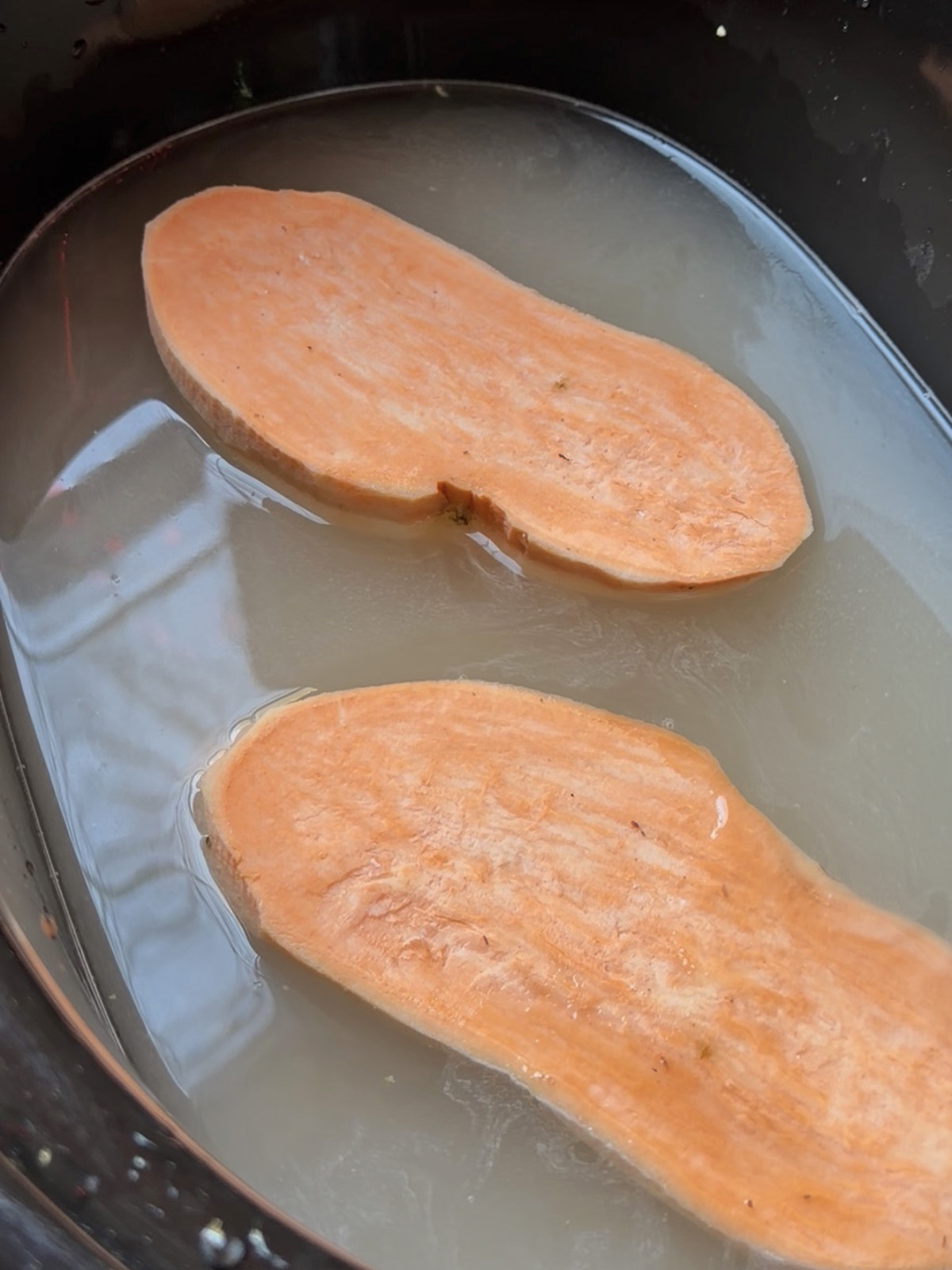 Two slices of sweet potato soaking in light-colored liquid in a pan.
