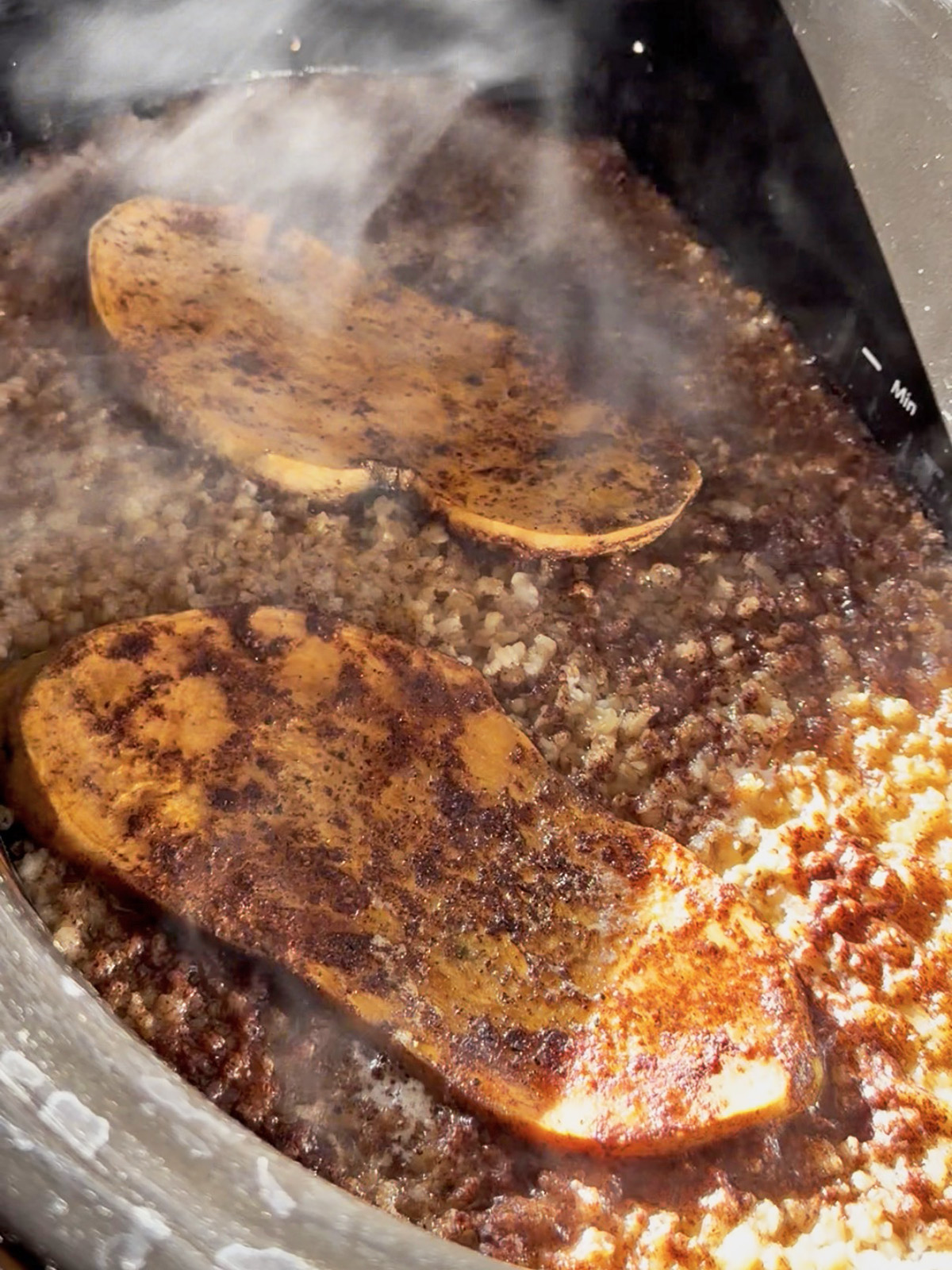 Slices of sweet potato cooking in a pot with oats and spices, steam rising.
