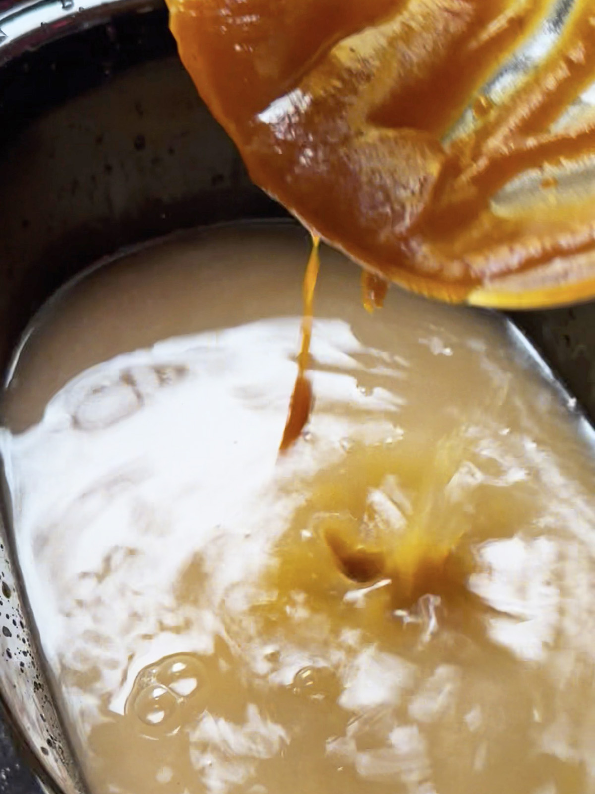 Creamy, pale oatmeal base with orange juice being poured in from a squeezed fruit.