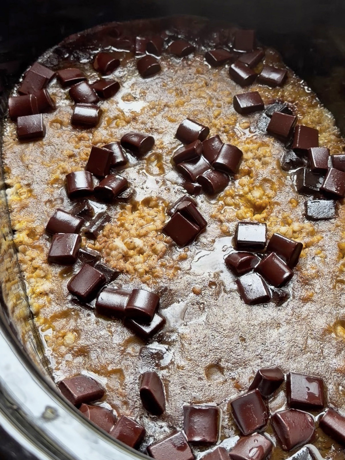 Chocolate chunks scattered on a caramelized oatmeal pudding with a glossy surface.