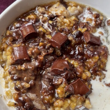 Creamy oats with chocolate chunks and caramelized fruit in a white bowl, spoon visible.