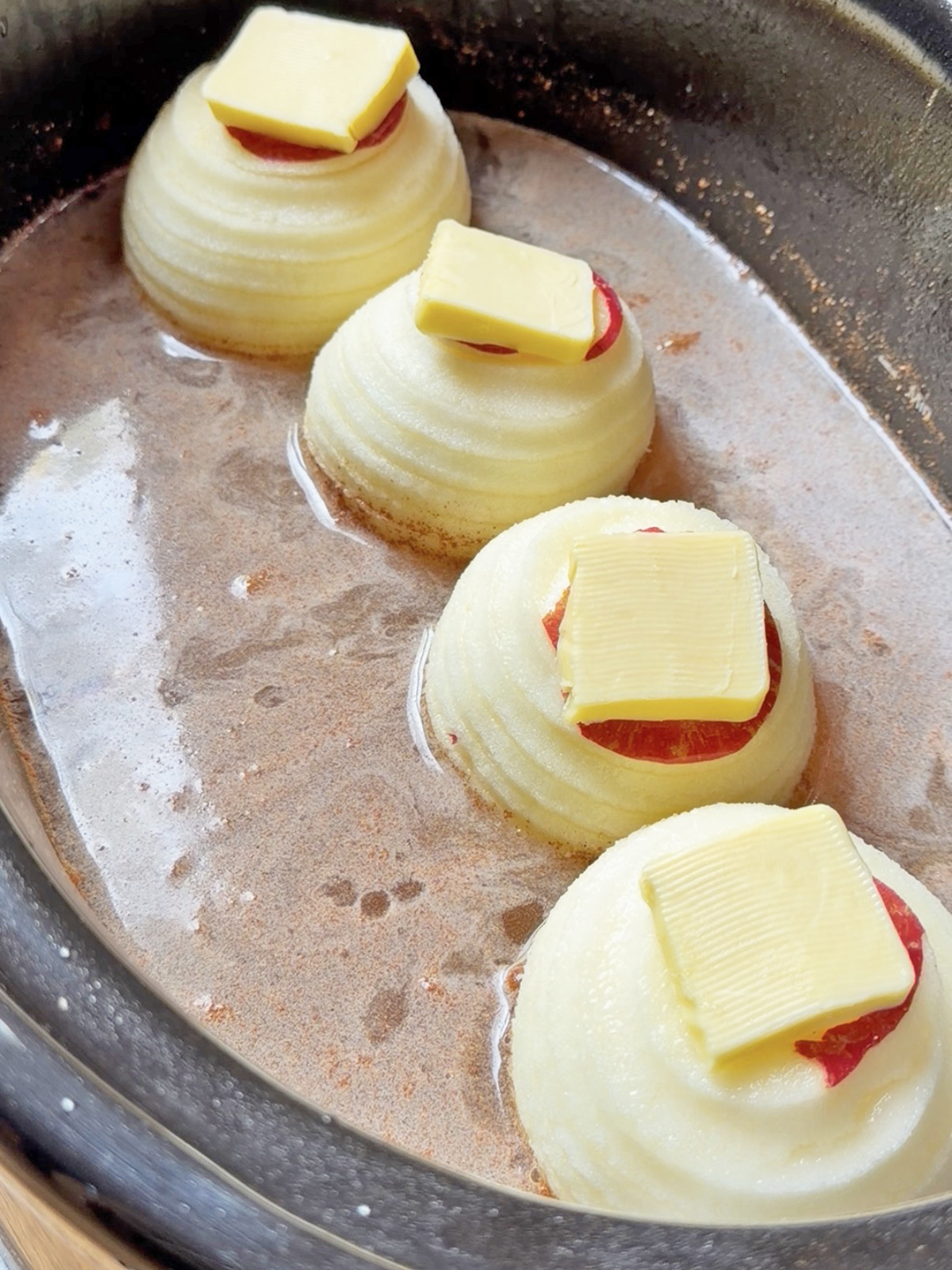 Onions with slices of cheese melting on top in a skillet.