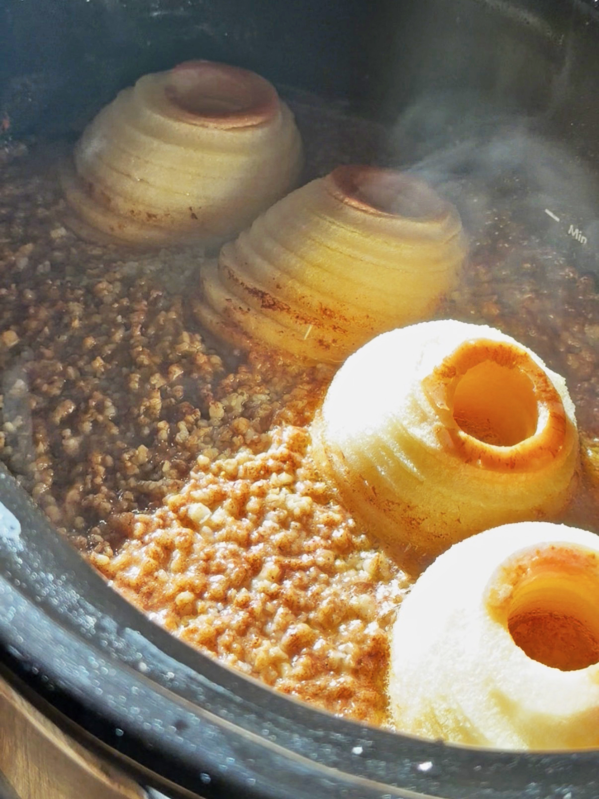 Three halved onions cooking in a crockpot with ground meat and sauce.