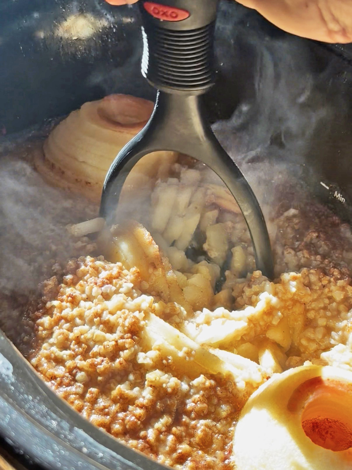 Cooking apple oatmeal in a slow cooker with a spoon stirring the mixture.