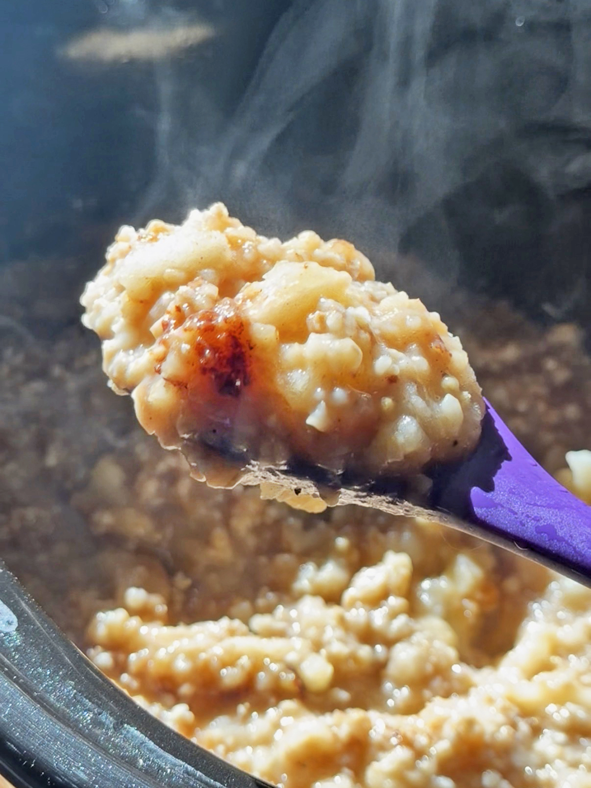 Steaming spoonful of cooked apple oatmeal in a slow cooker.