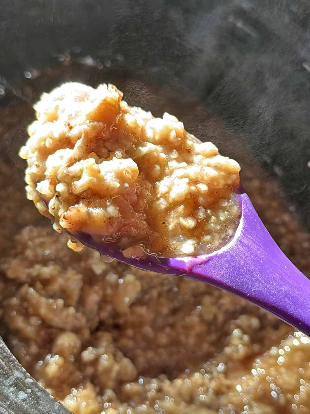 Close-up of cooked banana oatmeal in a purple spoon with a textured surface.